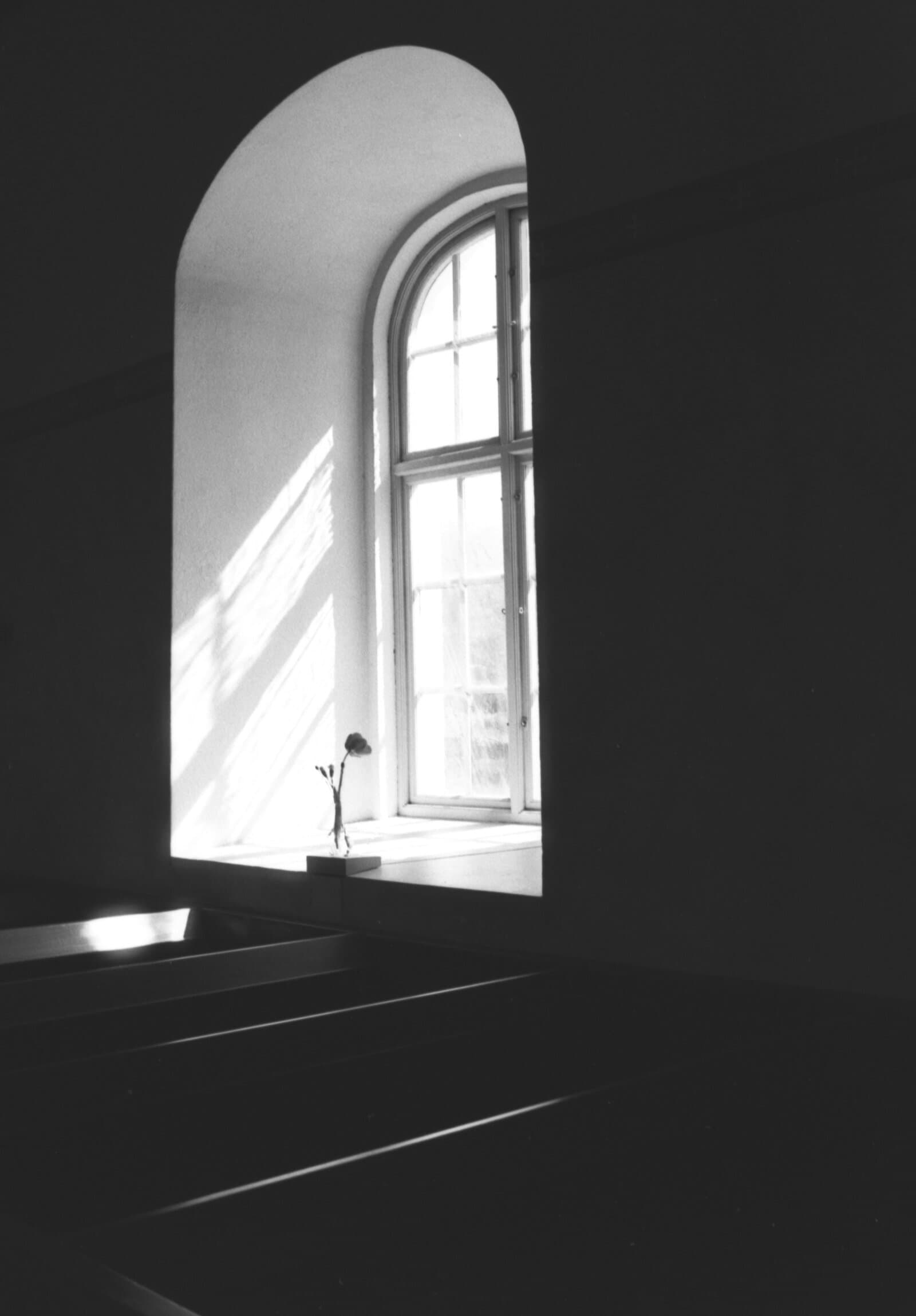 Sonnenlicht fällt durch ein Kirchenfenster auf leere Bankreihen